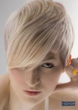 Asymericky střižený účes z krátkých rovných blond vlasů, s ofinou na straně